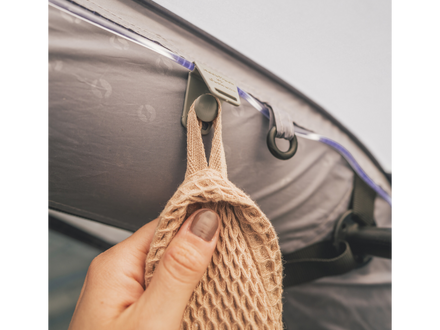 Hand holding a beige mesh bag over a car door handle.