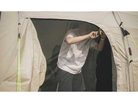 Person standing inside a beige tent with a white dog on a white background