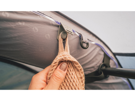 Hand holding a woven bag over a car window with hooks attached.
