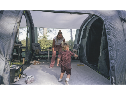 Two people inside a large camping tent with outdoor furniture visible