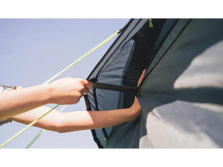 Person adjusting a tent flap with a clear blue sky background