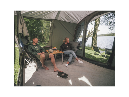 Two people sitting inside a tent by a lake, enjoying a picnic.