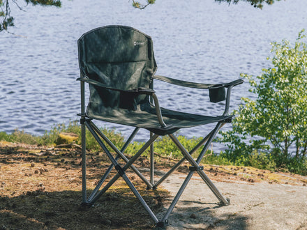 Foldable camping chair by a body of water with trees in the background