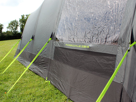 Gray camping tent with green stakes on a grassy field