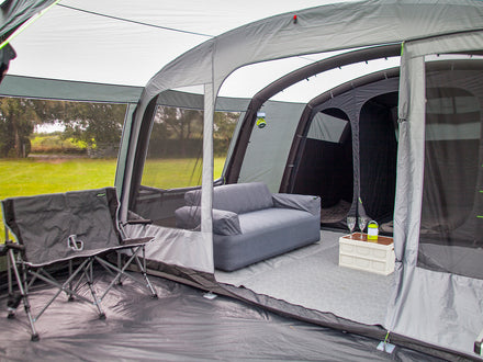 Camping trailer interior with gray furniture and open door showing outdoor view.
