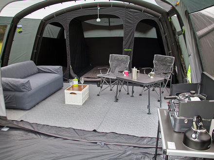 Camping setup inside a vehicle with a gray sofa, chairs, and a small table.