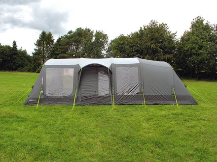 Large gray tent with mesh door on a grassy field with trees in the background