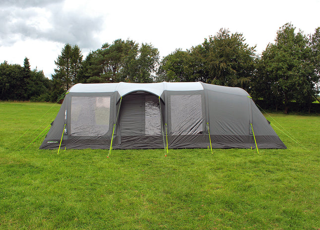 Large gray tent with mesh door on a grassy field with trees in the background