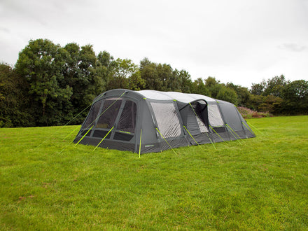 Large camping tent with attached screen porch on a grassy field with trees in the background