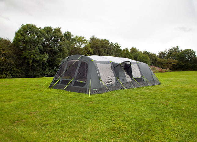 Large camping tent with attached screen porch on a grassy field with trees in the background