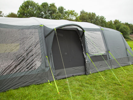 Gray inflatable tent with mesh door on a grassy field with trees in the background