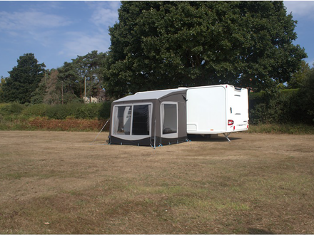 Caravan with an attached awning in a grassy area with trees in the background