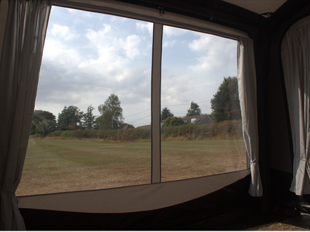 View from inside an awning with large windows showing a grassy field and trees.