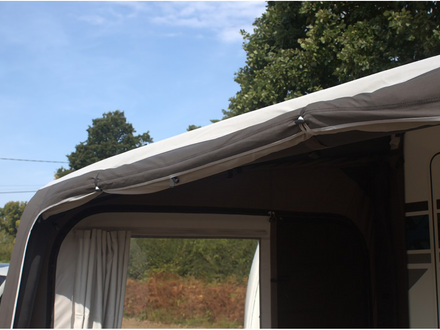 Caravan with an extended awning against a natural background of trees and blue sky.