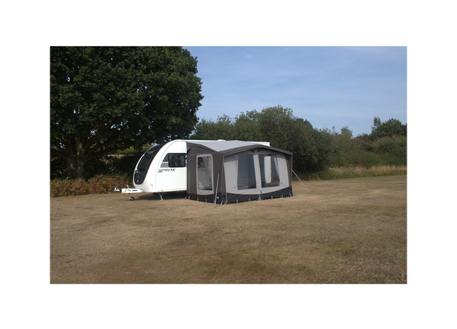 Caravan with an attached awning in a grassy field with trees in the background