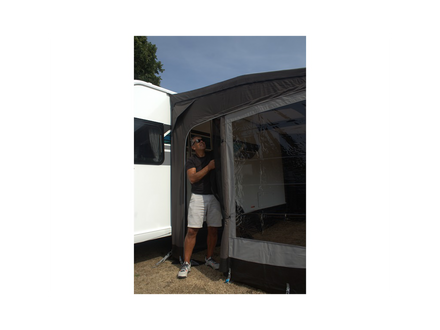 Person standing inside a caravan with an extended awning on a clear day.