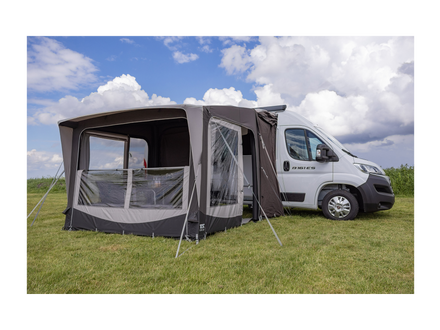 Camping trailer with an attached awning on a grassy field under a blue sky.
