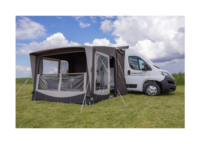 Camping trailer with an attached awning on a grassy field under a blue sky.