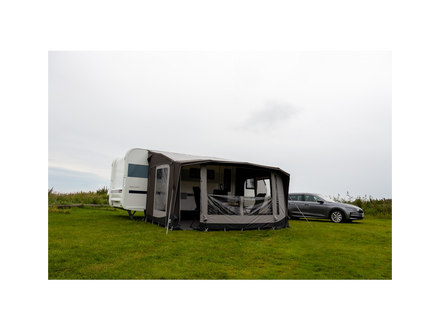 Caravan with an extended awning on a grassy field with a car in the background.