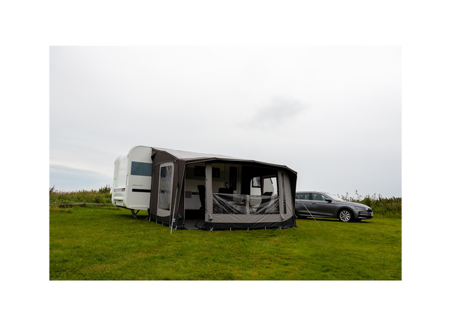 Caravan with an extended awning on a grassy field with a car in the background.
