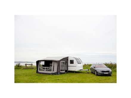 Caravan with an awning and a car parked nearby on a grassy field.