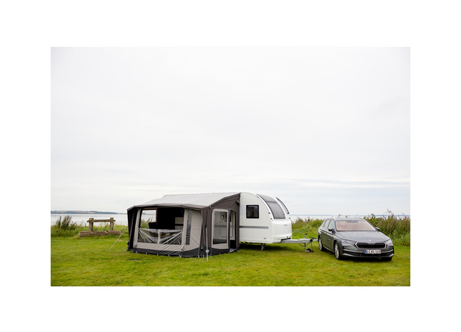 Caravan with an awning and a car parked nearby on a grassy field.