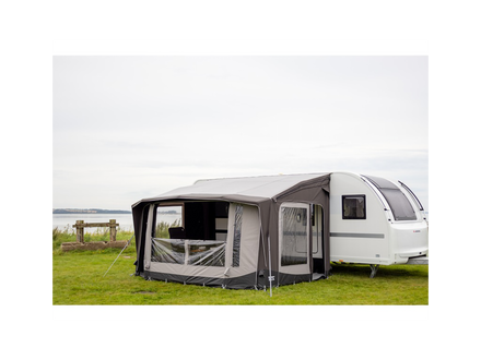 Caravan with an awning extended on a grassy area with a lake in the background
