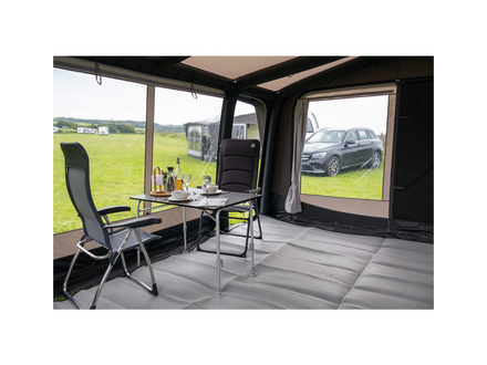 Interior of a caravan with chairs, table, and view of a car and landscape outside