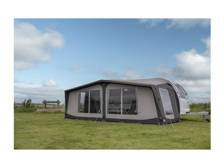 Caravan with an awning extended on a grassy field under a blue sky.