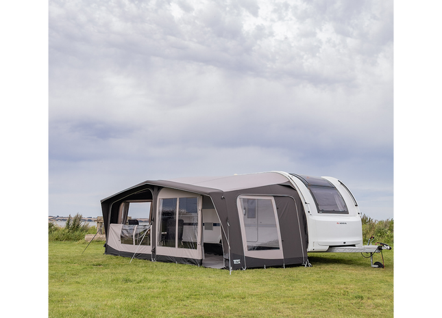 Caravan with an awning on a grassy field under a cloudy sky