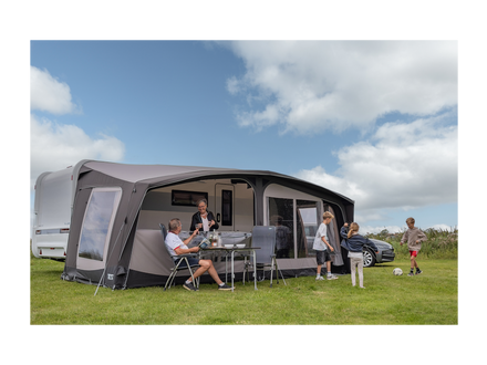 Family enjoying time outdoors next to a caravan with an awning on a grassy area.