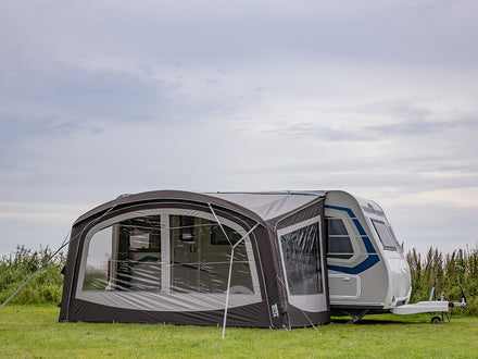 Caravan with an attached awning on a grassy field under a cloudy sky.
