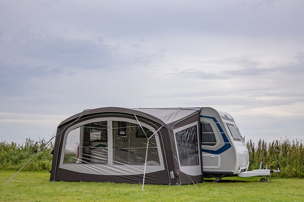 Caravan with an attached awning on a grassy field under a cloudy sky.