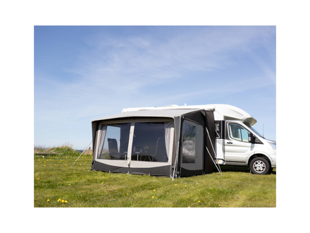 Camping trailer with an extended awning on a grassy field under a blue sky.