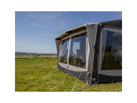 Caravan with an awning extended on a grassy field under a clear blue sky.