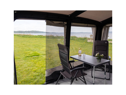 Inside a caravan with chairs and a table, looking out to a grassy field and water.