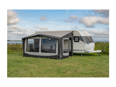 Caravan with an attached awning in a grassy field with a cloudy sky.