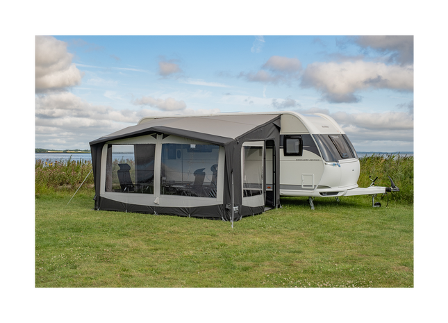 Caravan with an attached awning in a grassy field with a cloudy sky.