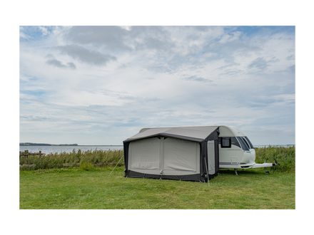Caravan with an awning set up on a grassy area with a cloudy sky.