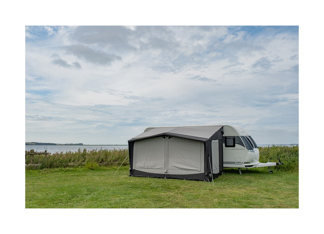 Caravan with an awning set up on a grassy area with a cloudy sky.