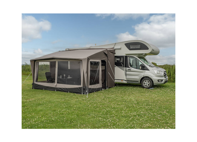Camper van with an extended awning on a grassy field under a blue sky.