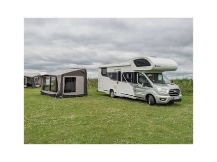 Camper van with an awning on a grassy field under a cloudy sky