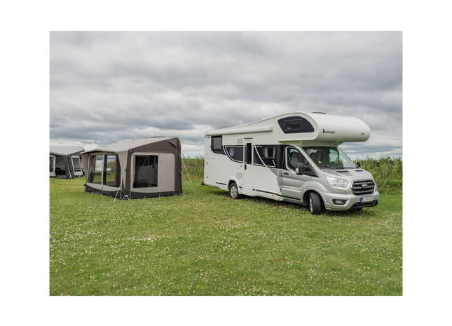 Camper van with an awning on a grassy field under a cloudy sky