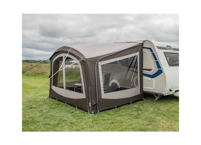 Caravan with an attached awning on a grassy field under a cloudy sky