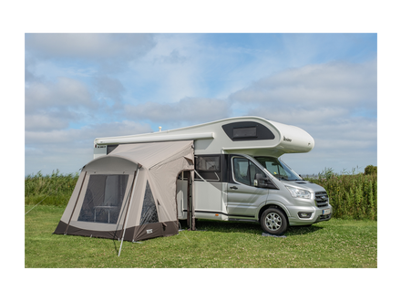 Van with an attached awningin a grassy area under a blue sky.