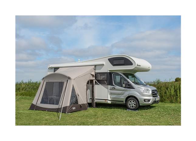 Van with an attached awningin a grassy area under a blue sky.