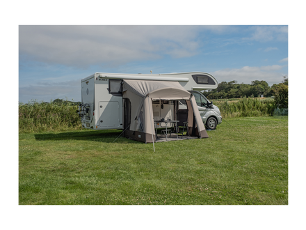 Camper van with an attached awning in a grassy field