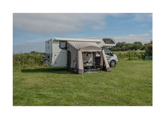 Camper van with an attached awning in a grassy field