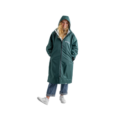 A woman wearing a long green hooded dryrobe with a white inner lining, blue jeans, and white sneakers, standing against a plain white background.