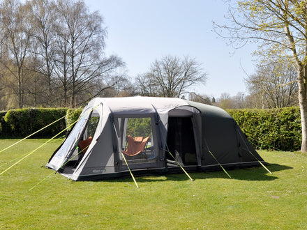 Gray camping tent with attached porch on a grassy area with trees in the background